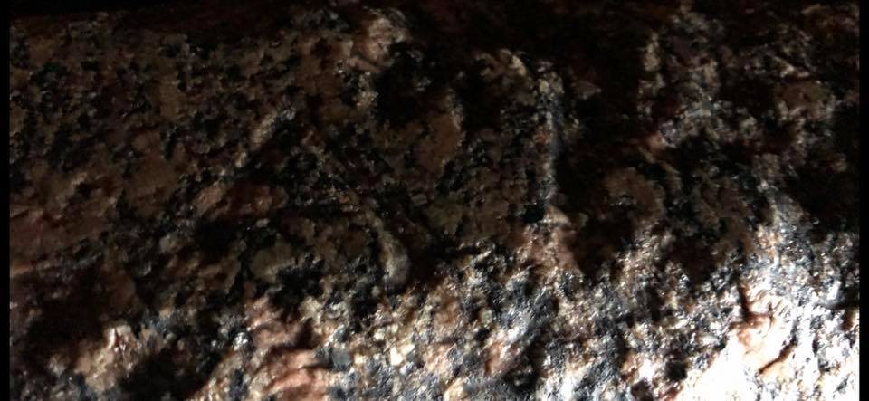 Close photograph of the granite rim of the box where the Alpha and Omega are pressed into the stone